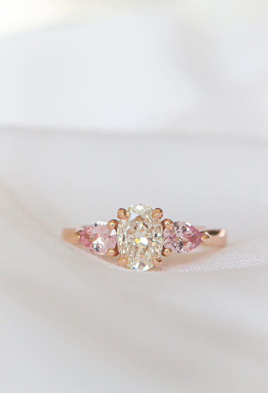 Rose gold ring with a large diamond and smaller pink gemstones on a white background